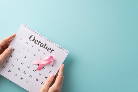 October's importance: First person top view of my hands arrange doctor's visit in the calendar, emphasizing breast cancer awareness. The pink ribbon on pastel blue background with empty space for textの写真素材