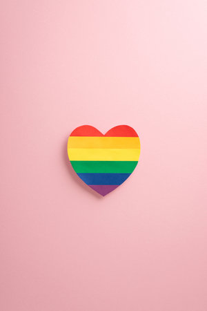 Immerse in LGBTQ+ Pride Month festivities. Witness a mesmerizing vertical top-down capture showcasing LGBTQ+ flag on heart shape on gentle pastel pink backdrop. Ad-friendly with copyspace providedの写真素材
