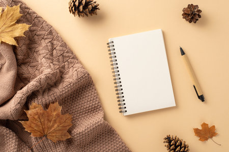 Fall-themed office setup: Overhead shot of warm knitted blanket, notepad, pen, maple leaves and pine...
