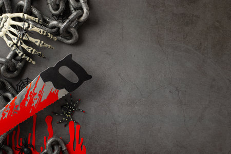 Sinister greeting concept: Top view of themed decor - creepy spiders, spiderweb, skeleton hand, blood traces, chain, saw against gritty concrete backdrop, text or advert room availableの写真素材