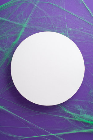 Mysteriously Creepy Halloween: vertical top-down view glimpse of themed decor, sinister green spiderweb over purple backdrop, blank circle for greeting message or advertisingの写真素材