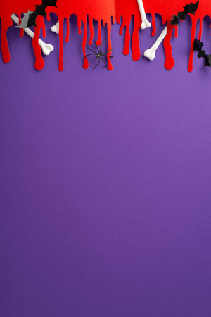 Embrace Halloween with imaginative arrangement. Vertical top view of thematic embellishments, eerie blood smears, skeletal fragments, spectral spider, bats on violet backdrop with space for text or adの写真素材