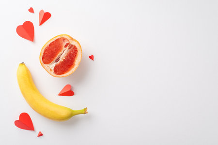 Understanding sexuality: top view shot of grapefruit half, symbolizing female genital, banana, evoking male anatomy, and hearts, set against white backdrop, providing space for text or promo contentの写真素材