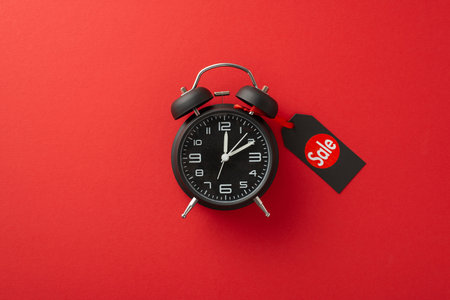 Tick-tock, Black Friday o'clock! A top view image of black alarm clock adorned with a 'sale' price tag on a red background, creating space for promotional text or advertisementsの写真素材