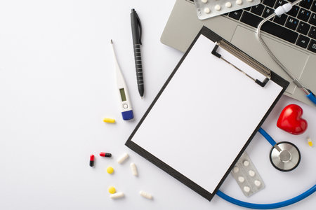 Virtual medical appointment concept. Overhead view of a laptop, stethoscope, medical questionnaire clipboard, pen, thermometer, pills on a white background with room for a text or adの写真素材