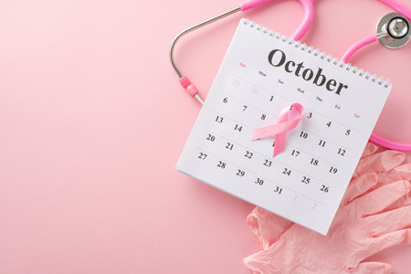 Breast cancer screening date. Top-view perspective of pink surgical gloves, stethoscope, and October calendar featuring pink ribbon on pastel pink setting, offering space for your messaging or advertの写真素材