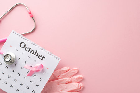 Breast cancer screening reminder. Overhead shot of pink surgical gloves, stethoscope, and October calendar featuring a pink ribbon on soft pink background, ready for your message or promotionの写真素材