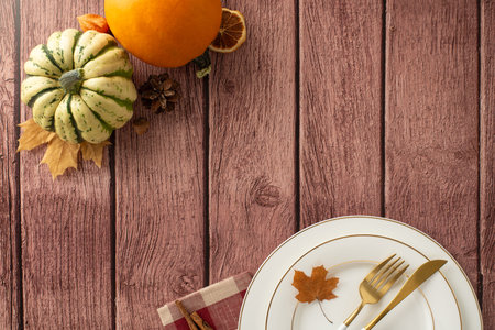 Aerial glimpse into fall-themed Thanksgiving dinner with family. Gilded plates, refined cutlery, and pumpkins adorn brown wooden isolated background, providing space for text or advertsの写真素材