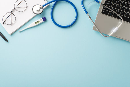 Discover convenience of online healthcare. Top view shot featuring laptop, stethoscope, patient's individual medical record, glasses, thermometer on pastel blue backdrop, customizable for your needsの写真素材
