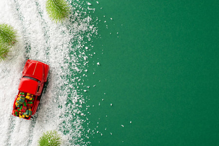 Winter Wonder: An overhead view of a small vintage red car laden with gifts weaving through a pine tree forest in the snow, creating space for your festive messages against green backgroundの写真素材