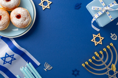 Engage in Hanukkah customs with a top-view shot showcasing sufganiyot, Star of David symbols, Israeli flag, gift box with ribbon bow, menorah on blue backdrop, offering space for text or promo contentの写真素材
