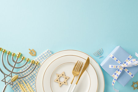 A top view photograph showing beautifully arranged table setting with plates, cutlery, napkin, the Star of David, giftbox, menorah candle holder, and other festive symbols on pastel blue backgroundの写真素材