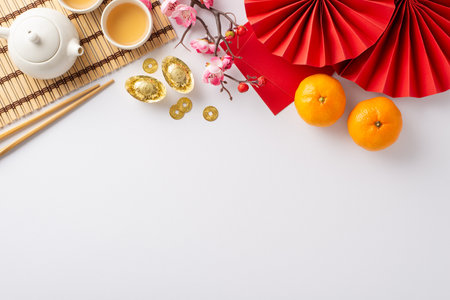 Unveil beauty of Chinese New Year through lavish table arrangement. Top view of intricate fans, green tea ceremony essentials, Feng Shui accents, fresh tangerines, sakura blossoms on white backdropの写真素材