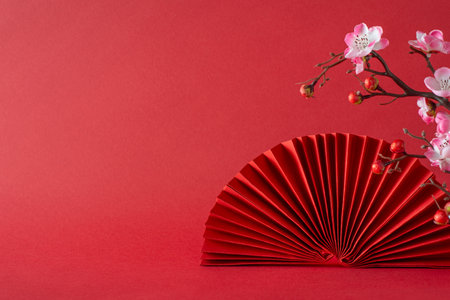 New Year symbolism: A side view composition featuring pink sakura blossoms, and fan. Against a red background, leaving empty space for text or promotional messagesの写真素材