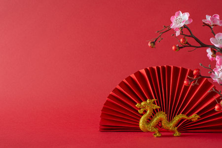 Cultural tableau: side view feng shui items, dragon, sakura blossoms, and fan create an elegant display on a table. The red background provides a vibrant space for text or adsの写真素材