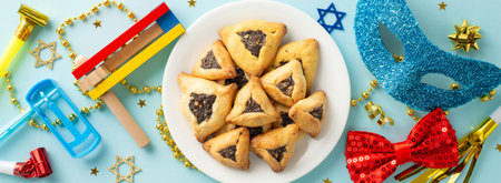 Top view of Purim festivity items: plate of filled triangle cookies, religious icons, and joyful...