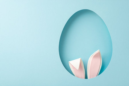 Playful Easter inspiration photo. Top view of humorous bunny ears peeking from an ovoid gap on a tranquil blue setting, with space for your textの写真素材