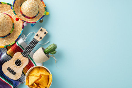 Cinco de Mayo setup from top view, featuring iconic accessories like sombreros, vihuela, cactus, a bright serape, and nachos, placed on a pastel blue canvas with area for textの写真素材
