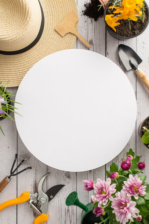 Get your hands dirty in spring garden scene. Top view vertical shot showing young blooms, sunhat, gardening gear arranged on wooden background. Invitation to nurture nature. Empty circle for advertの写真素材