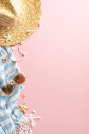 Vertical flat lay of summer vacation accessories, including a straw hat, sunglasses, blue and white scarf, and sea stars on a pink background, invoking the joy of travelの写真素材