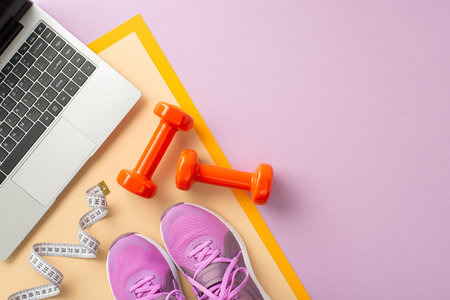 Top view of fitness equipment including dumbbells, sneakers, and a laptop with measuring tape on colorful backgroundの写真素材