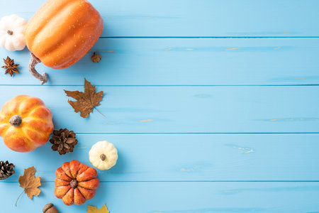 Top view of assorted autumn pumpkins, pinecones, and leaves on a blue wooden background. Ideal for seasonal and Thanksgiving themesの写真素材