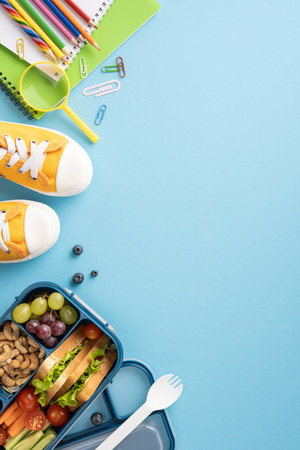 Top vertical view of a healthy school snack, yellow sneakers, and colorful stationery on a blue...