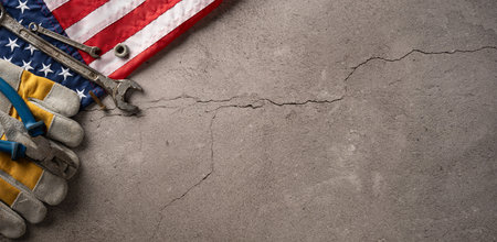 Tools and protective gloves arranged next to the American flag on a rough concrete surface representing Labor Dayの写真素材