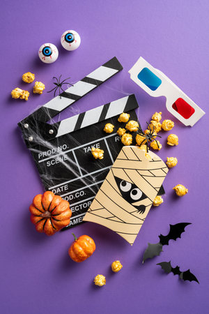 Creative Halloween movie night setup with popcorn, pumpkins, spooky decorations, and 3D glasses on a vertical purple backgroundの写真素材