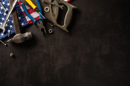 Labor Day concept featuring traditional hand tools and the American flag on a dark surface,...