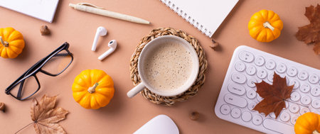 A cozy autumn-themed workspace featuring a coffee cup, mini pumpkins, and office supplies creating a...