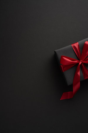 A stylish vertical black gift box wrapped with a striking red ribbon on a dark background, perfect for celebrations and special occasionsの写真素材