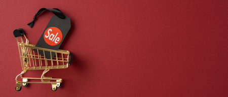 A golden shopping cart with a sale tag on a red background conveying the concept of discounts and salesの写真素材