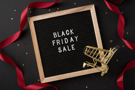 Black Friday sale sign with a golden shopping cart and red ribbon on a festive backdrop, symbolizing holiday salesの写真素材