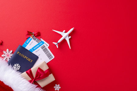 Top view of a holiday travel setup featuring a passport, boarding passes, gift, and airplane over a red background, symbolizing festive travel plansの写真素材