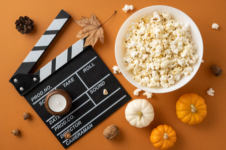 Flat lay of popcorn, pumpkins, and a clapperboard on an orange background symbolizing an autumn movie night atmosphereの写真素材