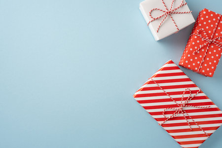 Three beautifully wrapped Christmas presents with red and white designs are arranged on a light blue surface, creating a festive and joyful atmosphereの写真素材