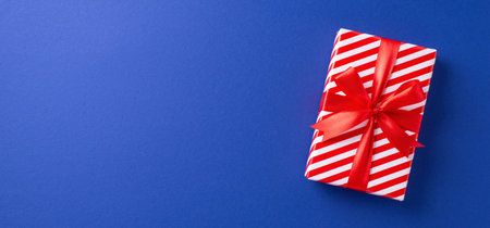 A beautifully wrapped Christmas gift box with red and white stripes tied with a red ribbon, set against a vibrant blue background. Perfect for festive and holiday themed imageryの写真素材