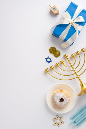 A festive Hanukkah vertical scene featuring a golden menorah, blue gift box, Star of David, dreidel, and donut. Celebration and traditional Jewish holiday items arranged on a white surfaceの写真素材