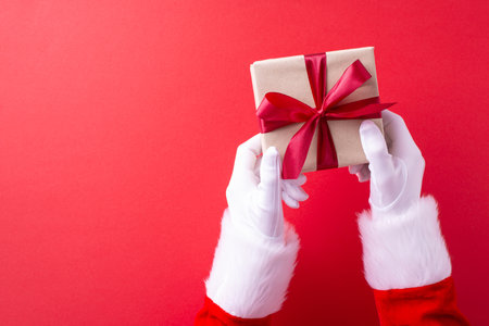 Santa Claus hands presenting a beautifully wrapped Christmas gift against a red background, conveying a festive and joyful holiday spiritの写真素材