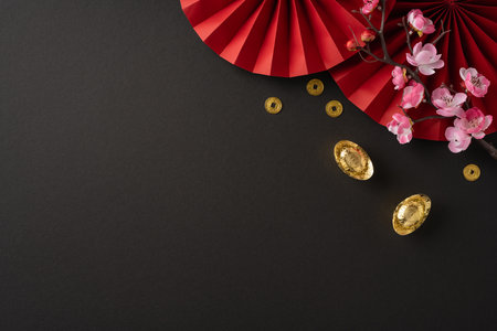 Festive Chinese new year composition featuring red decorations, blooming cherry blossoms, and gold ingots symbolizing prosperity and good fortune on a dark backgroundの写真素材