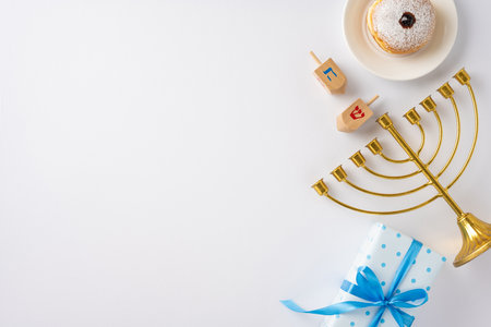 Festive Hanukkah scene featuring a golden menorah, traditional dreidels, jelly donut, and a wrapped gift with blue ribbon on a white backgroundの写真素材