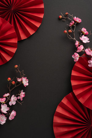 Aesthetic vertical arrangement of red paper fans and cherry blossoms on a black background, symbolizing Chinese New Year traditions and eleganceの写真素材