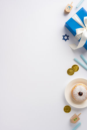 Festive Hanukkah vertical composition featuring a blue wrapped gift, dreidel, chocolate gelt, and a powdered sufganiyah on a white background, creating a warm celebration atmosphereの写真素材