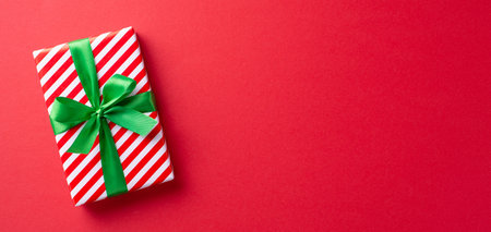 A beautifully wrapped gift box with a green ribbon is placed on a vibrant red background, evoking a festive and joyful Christmas spiritの写真素材