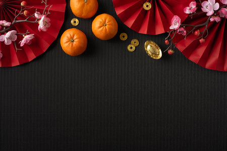 Chinese New Year decorations with red fans, tangerines, and gold ingot on a dark background symbolizing prosperity and festivityの写真素材
