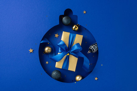 A beautifully wrapped flat lay gift with a blue ribbon sits among festive decorations on a blue background, creating a perfect winter holiday sceneの写真素材