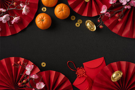 Top view of Chinese New Year decorations including oranges, red envelopes, and gold ingots on a black backgroundの写真素材