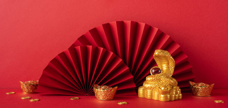 Red and gold decorations symbolize the Chinese New Year 2025, featuring a golden snake, fans, and coins on a vibrant backgroundの写真素材