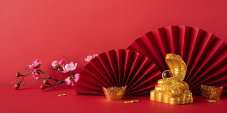 Festive image featuring a gold snake and red fans symbolizing Chinese New Year 2025. Red background enhances the cultural significance and prosperity theme, alongside floral, gold coin decorationsの写真素材